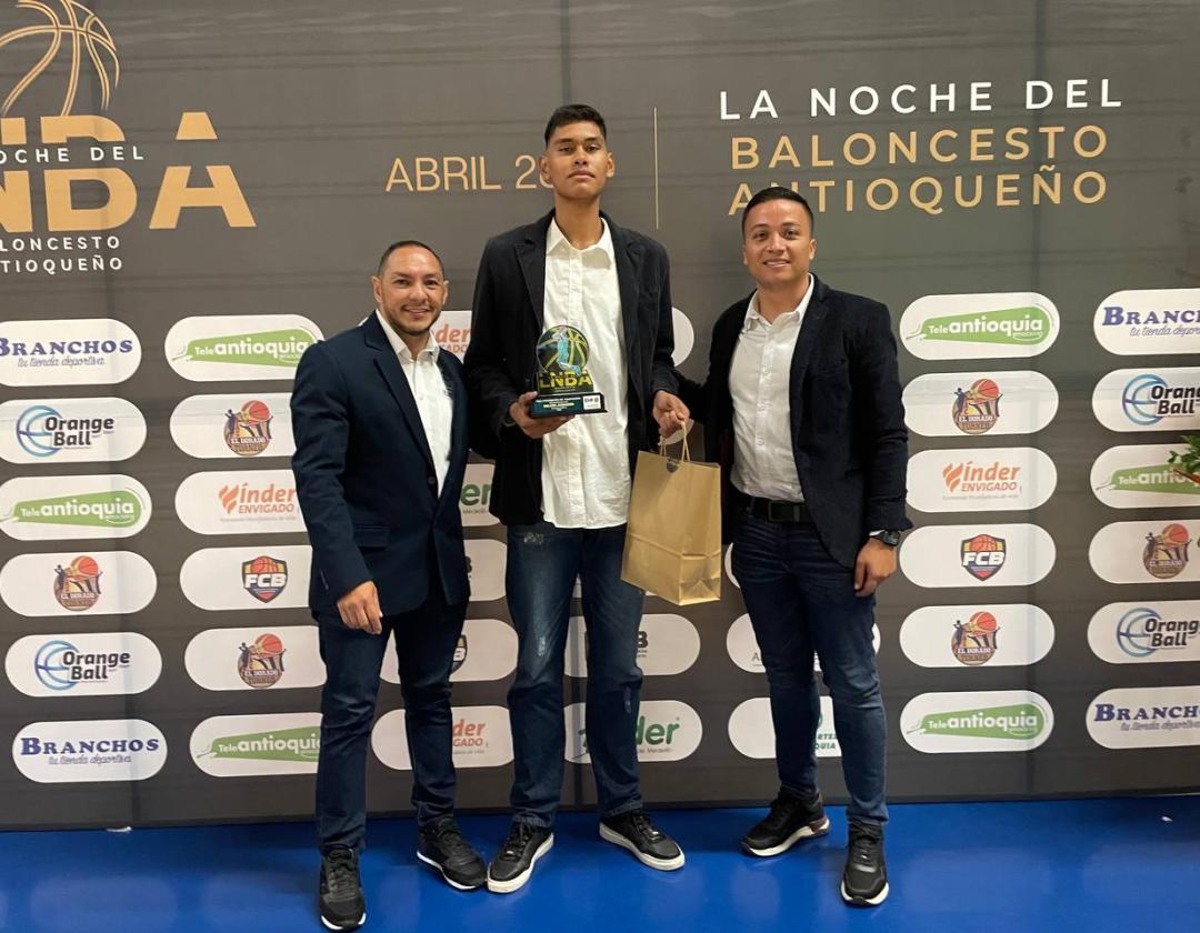 Deportista de Itagüí con servidores públicos en la ceremonia de reconocimiento mostrando el trofeo